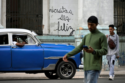 Des Cubains marchent devant le graffiti "Necesitas ser feliz" (Tu dois être heureux) du graffeur cubain Mr. Sad, à La Havane, le 12 décembre 2024