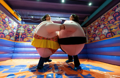 Des visiteuses, en costumes rembourrés, se battent dans l'"arène de sumo" au musée du rire HaHaHouse à Zagreb, le 21 janvier 2025 en Croatie