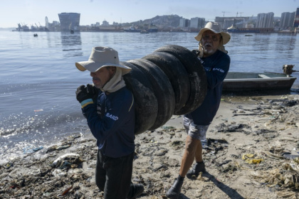 Des pêcheurs ramassent des pneus sur une plage de l'île de Pombeba, dans la baie de Guanabara, le 17 février 2025 à Rio de Janeiro, au Brésil