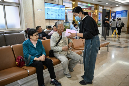 Meng Jia (d), une accompagnatrice de patient, prend en charge Gao Yingmin (g) et Tian Yigui (c) pour les guider dans un hôpital à Pékin, le 22 mai 2025 - Jade GAO (AFP)
