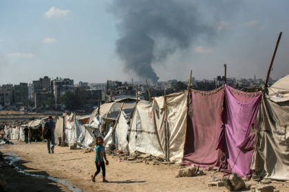 Des Palestiniens devant des tentes à Gaza-ville avec en arrière-plan une colonne de fumée s'élevant du centre de la bande de Gaza après un bombardement israélien, le 6 juillet 2025 - Bashar TALEB (AFP)