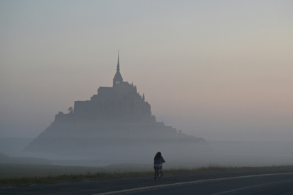 Un cycliste passe devant le Mont-Saint-Michel, enveloppé par la brume matinale, le 9 juillet 2025 - Damien MEYER (AFP)