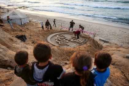 Des enfants regardent une sculpture de sable proclamant "Bienvenue au ramadan", le 17 février 2026 sur une plage au sud de la bande de Gaza - Eyad Baba (AFP)