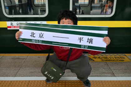 Un homme brandit une banderole "Pékin-Pyongyang" devant le train K27 à destination de Pyongyang, à la gare de Pékin, le 12 mars 2026 en Chine - ADEK BERRY (AFP)