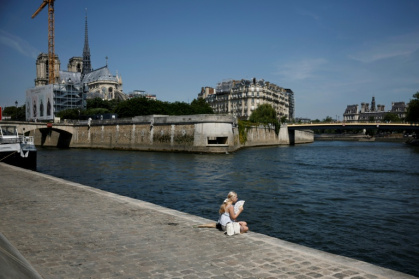 Une femme, assise sur les quais de la Seine, se rafraîchit avec un éventail lors d'une vague de chaleur précoce, le 28 mai 2026 à Paris - SIMON WOHLFAHRT (AFP)