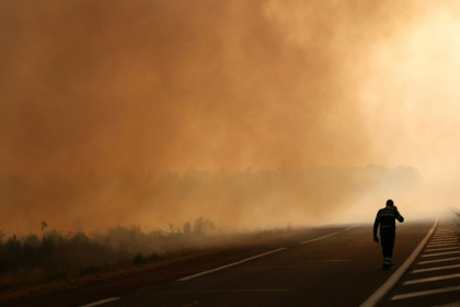 Un pompier marche sur une route à la lisière d'une zone en feu à Ares, le 26 juillet 2026, alors qu'un incendie de forêt ravage la forêt au nord du bassin d'Arcachon (Gironde) depuis le 22 juillet - ALAIN JOCARD (AFP)